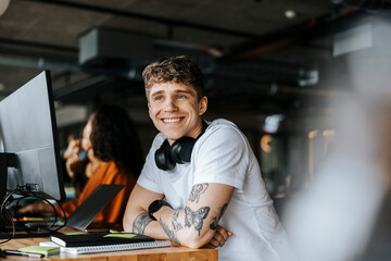 Smiling young male entrepreneur looking away while leaning at desk in office