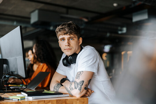 Portrait of young male entrepreneur leaning on elbows at desk in office