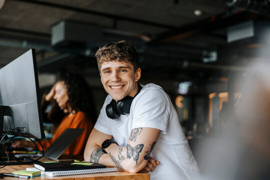 Portrait of smiling male programmer leaning on elbows at desk in office