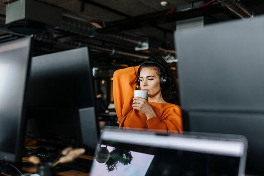 Young female computer programmer having coffee during break time at office