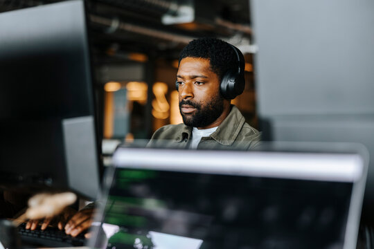 Focused male programmer working with wireless headphones at office