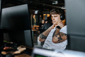 Young male entrepreneur with tattooed arms taking break while sitting at office