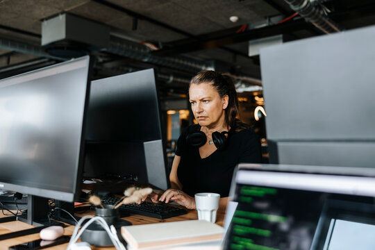 Mature female entrepreneur coding on computer while sitting at desk in office