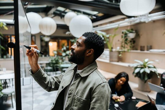 Male entrepreneur writing with felt tip pen on whiteboard in meeting at office