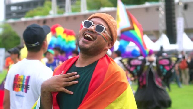 Happy young asian man with pride movement LGBT wrapped in rainbow flag for freedom. Demonstrate rights LGBTQ celebration pride Month gay pride symbol. Bangkok Pride Month festival.