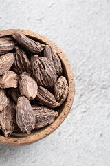 Dried Indian spice black cardamom in wooden bowl close-up on gray background top view with copyspace