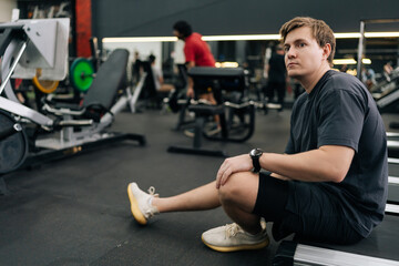 Handsome exhausted runner taking break at gym sit on treadmill. Portrait of exhausted sweaty male hard breathing after cardio exercise running workout. Weary man sit on fitness treadmill relax.