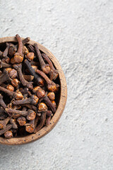 Dried Indian spice clove in wooden bowl close-up on gray background top view with copyspace