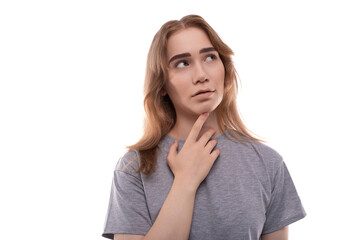 A blonde teenage girl of European appearance in a gray T-shirt is puzzled by solving a problem against a background of copy space