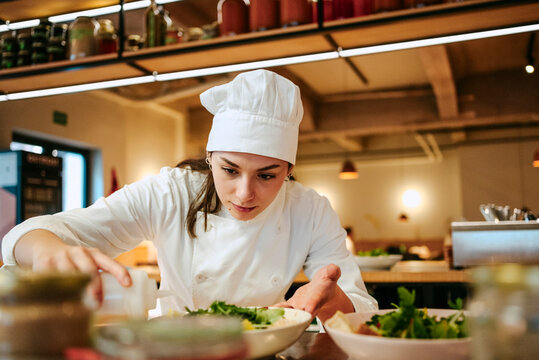 Close-up of female chef pouring dressing oil on salad at commercial kitchen