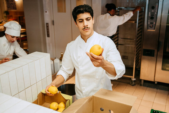 Male chef checking quality of lemon while standing in commercial kitchen