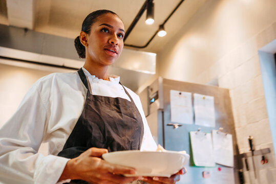 Low angle view of female chef with salad bowl walking in commercial kitchen
