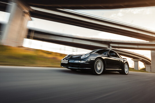Motion shot of black Porsche 911 Carrera coupe. Porsche 997 driving under the bridge at sunset. Kyiv, Ukraine - September 18 2016.