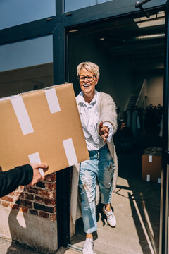 Happy female owner taking cardboard box from colleague at clothing store