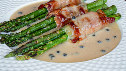 cooked fried asparagus with bacon with sauce, on plate
