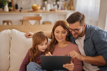 Curious little girl using the tablet with her parents in the living room
