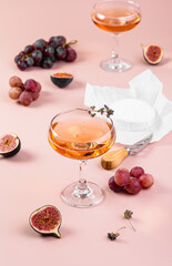 Refreshing rose wine in a glass with brie cheese, figs and grapes on a pink background