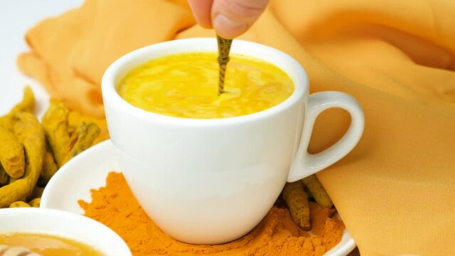Golden milk with turmeric in a cup, stirring the drink with a spoon, slow motion.