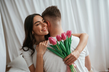 Pink flowers in hands. Young couple are together at home