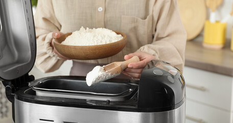 Making dough. Woman adding flour into breadmaker machine, closeup