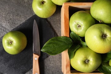 Ripe green apples with water drops, cutting board and knife on grey table, flat lay