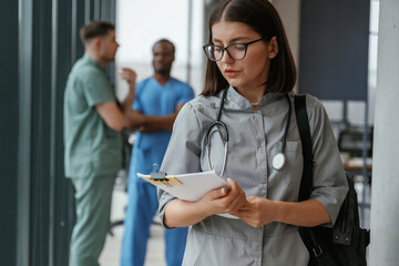 Beautiful woman in glasses is standing. Group of doctors are together indoors