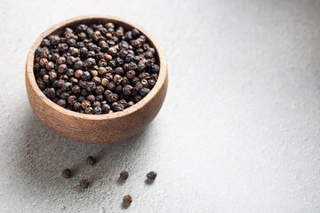 Indian spice black pepper in wooden bowl on gray background with copyspace