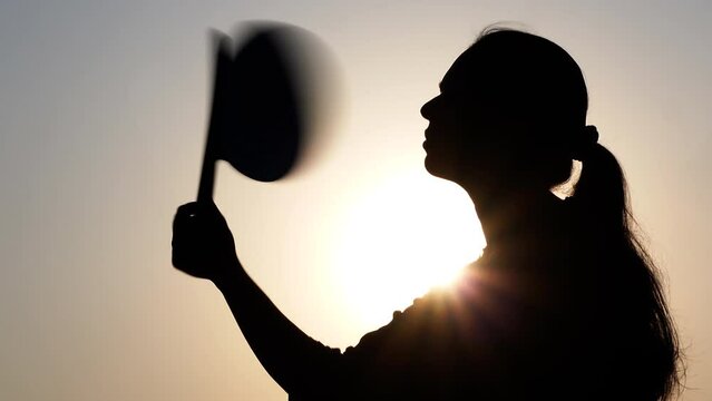 A woman sitting under the hot sun tries to cool her body using a hand fan.