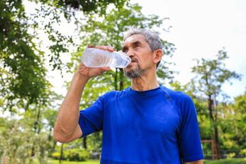 Senior Asian man is drinking water after morning exercise in the park for rehydration of sweat loss...