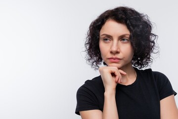 Caucasian woman with black curls looks slyly on a white background with copy space