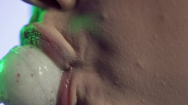 Makro zbliżenie z profilu kobiety oblizującej okrągły lizak, zabawa cukierkiem, białe tło, zielono-niebieska poświata na twarzy, sensualność, detal ust, kolor, smak i ekspresja