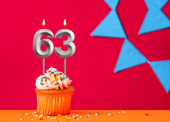 Birthday cupcake with candle number 63 on a red background with blue pennants