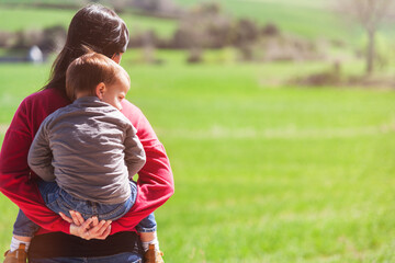 Woman taking her son to piggyback ride while watching green meadows. Family, leisure time.