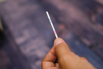 Woman hand holding positive pregnancy test strips on wood background