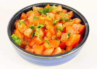 Tomatoes chopped in cubes with parsley in a blue ceramic bowl in white background