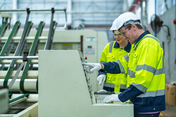 Male and female engineers in neat work clothes prepare and control the production system of large modern machines in a factory producing industrial technology products.