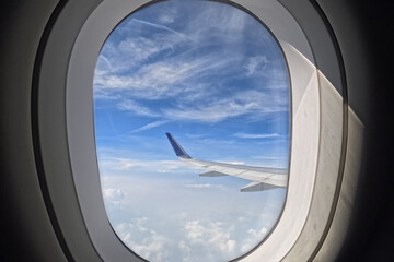 View of airplane wings in clouds through porthole. Blue sky background. Beautiful clouds and...