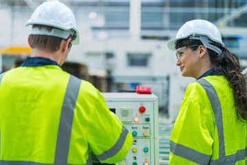 Male and female engineers in neat work clothes prepare and control the production system of large modern machines in a factory producing industrial technology products.