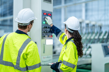 Male and female engineers in neat work clothes prepare and control the production system of large modern machines in a factory producing industrial technology products.
