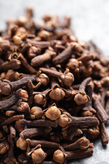 A close-up of dried cloves scattered on a textured light gray surface, Indian Indonesian spice.