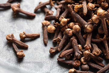 A close-up of dried cloves scattered on a textured light gray surface, Indian Indonesian spice for cooking and baking.