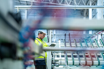 Fototapeta premium Male and female engineers in neat work clothes prepare and control the production system of large modern machines in a factory producing industrial technology products.