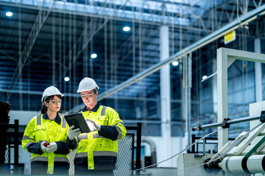 Male and female engineers in neat work clothes prepare and control the production system of large modern machines in a factory producing industrial technology products.