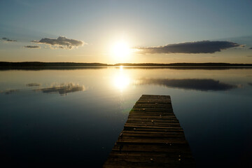 Obraz premium Wooden footbridge and sun reflecting in water at sunset