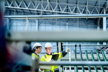 Fototapeta premium Male and female engineers in neat work clothes prepare and control the production system of large modern machines in a factory producing industrial technology products.