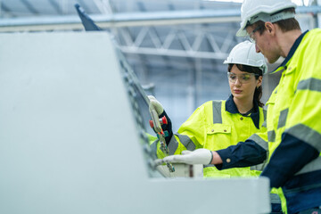 Male and female engineers in neat work clothes prepare and control the production system of large modern machines in a factory producing industrial technology products.