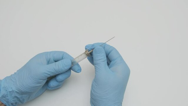 doctor wearing medical gloves puts metal needle on old glass reusable syringe, slow motion
