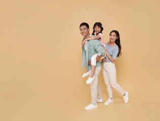 Full body portrait happy asian family standing giving piggyback ride to daughter, sit on back isolated on nude color background.