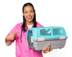 Young Filipina vet holding pet carrier smiling and pointing aside, showing something at blank space.