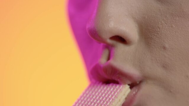 Makro zbliżenie młodej kobiety bez makijażu jedzącej wafelka i oblizującej usta na ż&oacute;łtym tle &mdash; slow motion 4K, radość, naturalność i apetyczny moment w studio